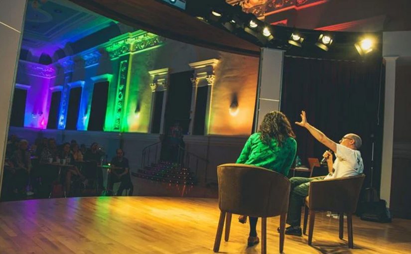 Two people sit on stage hosting a talk